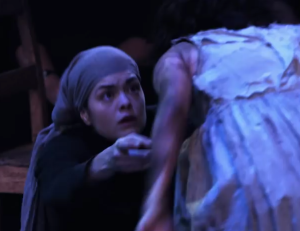 Abigail Williams (Samantha Colley) tells Betty Parris (Marama Corlett) what she must not confess, in Act One of The Crucible. Source: screencap of DigitalTheatre vid.
